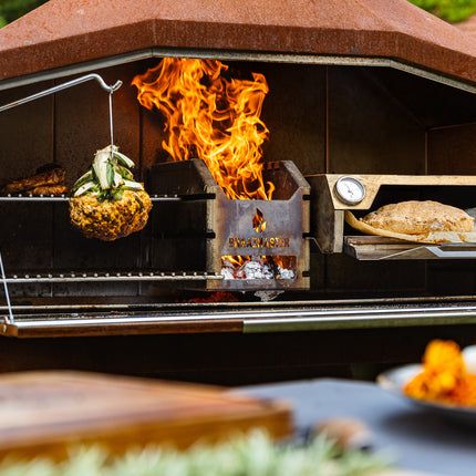 Braaimaster Duo Corten, geopend, vooraanzicht met vuur in de firebok en een braaioven op het rooster plus gegrilde bloemkool aan de haak