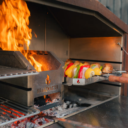 Braaimaster Diuo Corten interieur met vuur in de firebox en churrasco spiesen op het rooster
