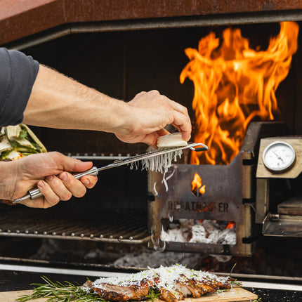 Braaimaster Duo Corten met viuur in de firebox en op de klep een steak & cheese waar kaas overheen geraspt wordt