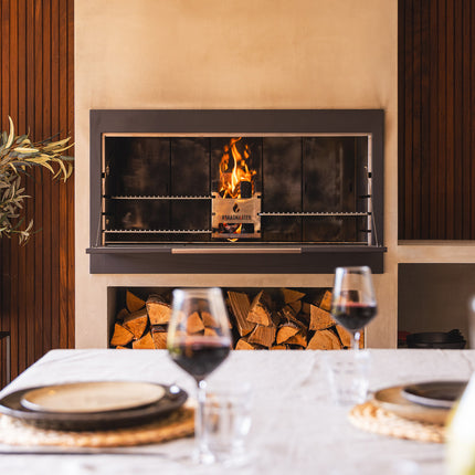 Braaimaster Duo black ingebouwd in zandkleurige schouw, brandend, glazen schuifwand en gedekte tafel