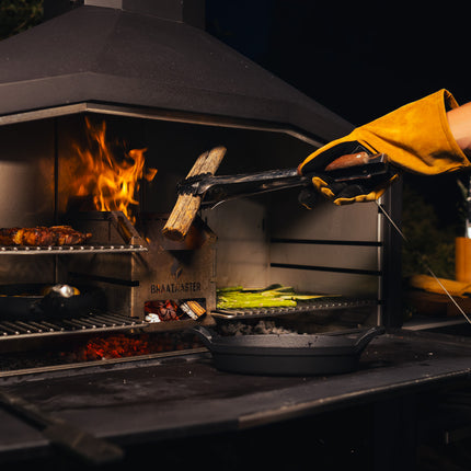 Braamaster Duo Black met gloeiende kolen, gevulde roosters en een braaimaster legt een blok sekelbos in de vuurbox