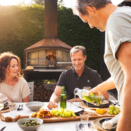 Braaimaster Duo Corten brandend op de achtergrond met op de voorgrond een gevulde dinertafel