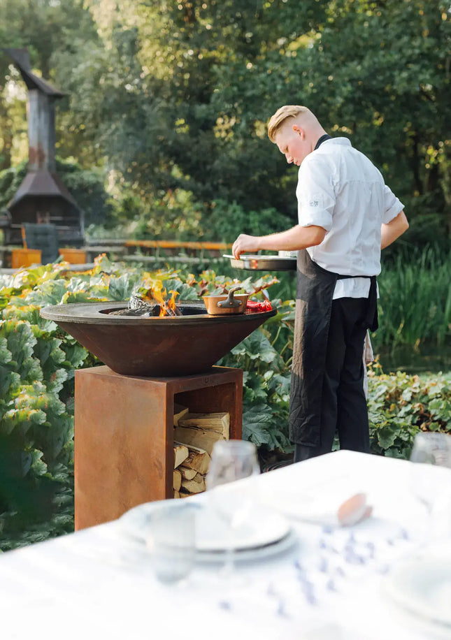 OFYR Heritage Classic Storage 100 Corten in tuin met chef  en pannetje op de plancha en een braai in de achtergrond