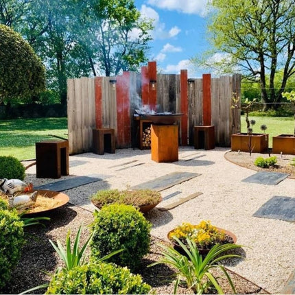 OFYR Classic 85 heritage corten vuurschaal met rokend vuur in de tuin tegen schutting achtergrond