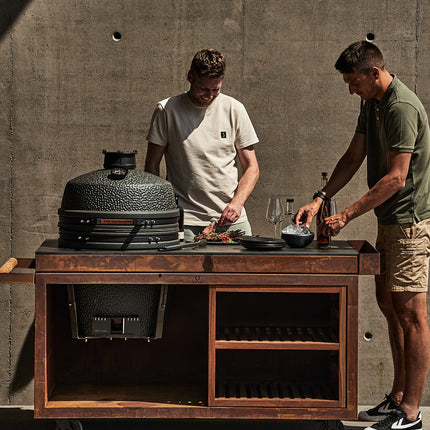 The Bastard kamado VX Large Solo ingebouwd in een corten stalen tafel met personen die eten voorbereiden